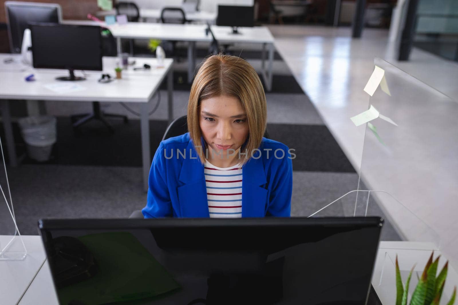 Asian businesswoman sitting in office in front of computer near sneeze shield by Wavebreakmedia