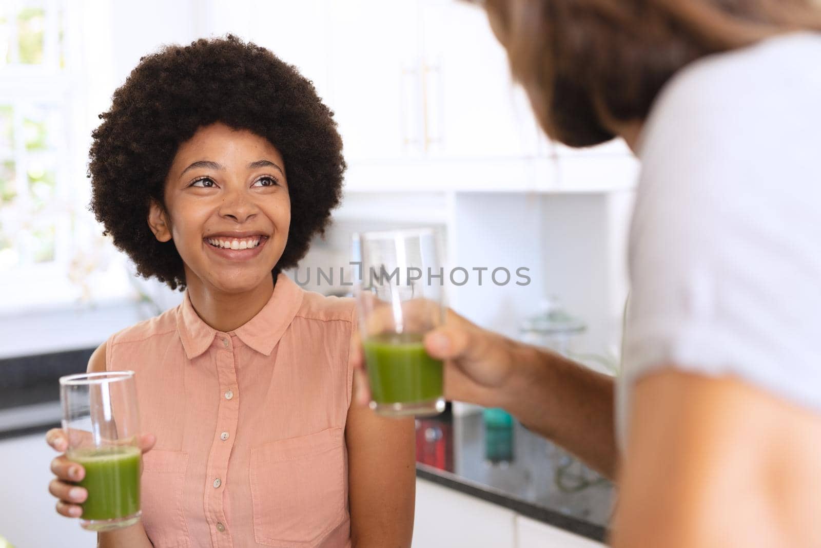 Happy diverse couple in kitchen smiling and drinking health drink. staying at home in isolation during quarantine lockdown.