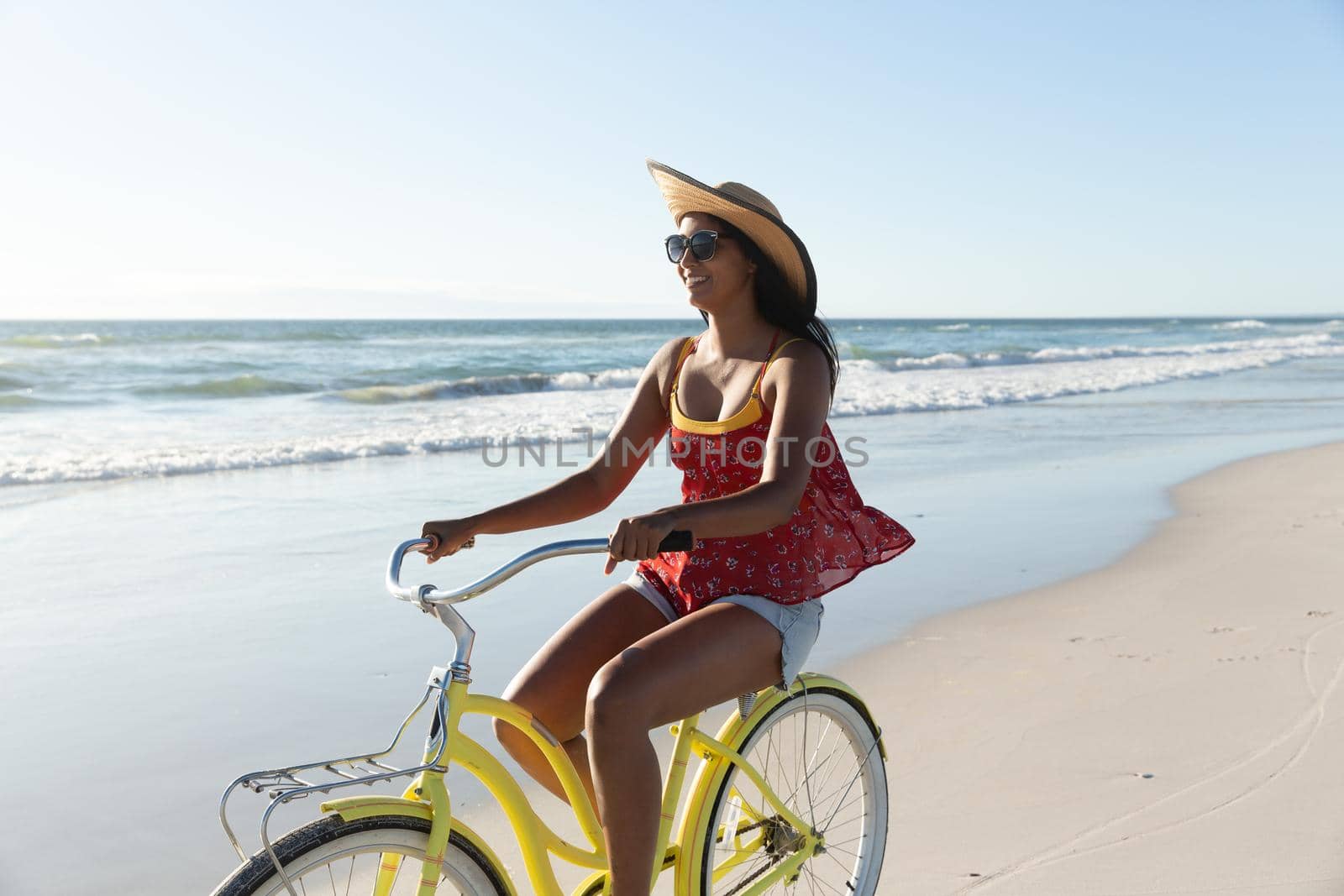 Happy mixed race woman on beach holiday riding bicycle on the sand by the sea by Wavebreakmedia