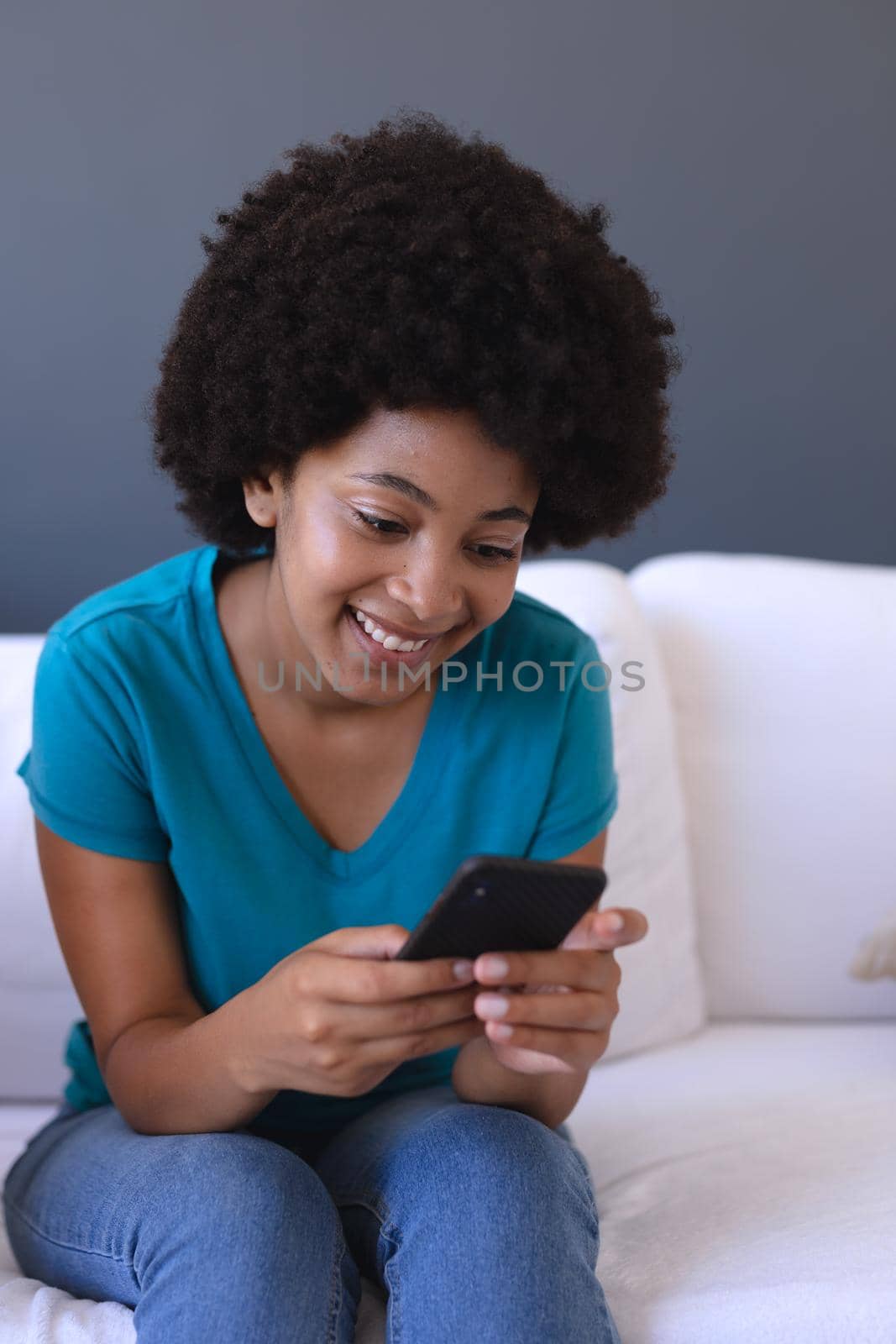 African american woman sitting on sofa using smartphone by Wavebreakmedia