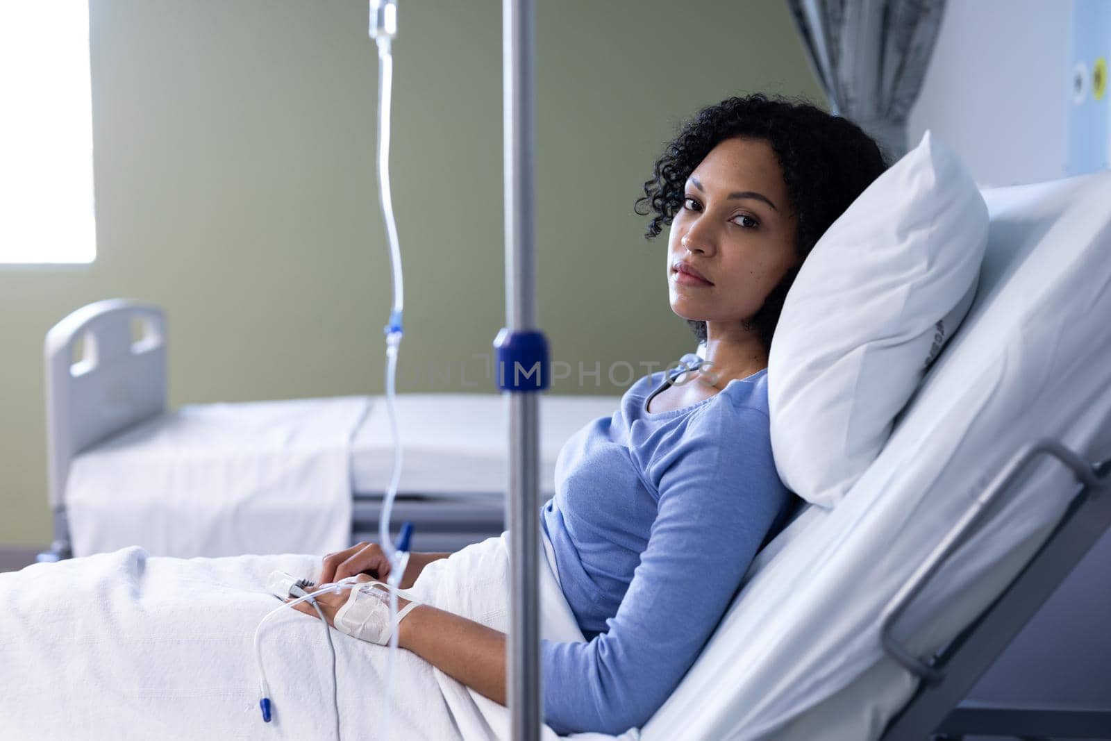 Mixed race female patient sitting in hospital bed wearing fingertip pulse oximeter and iv drip by Wavebreakmedia