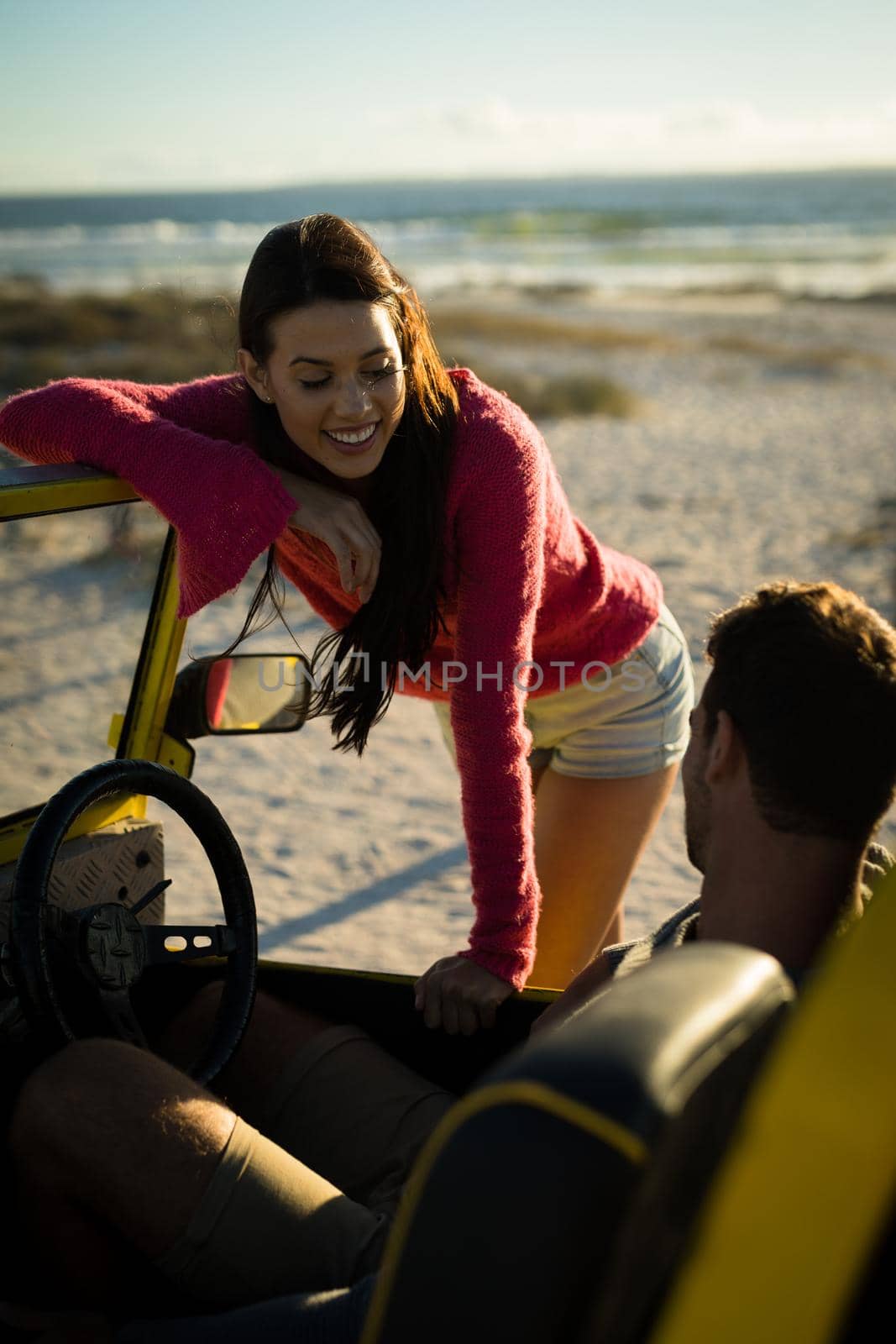 Happy caucasian couple on beach woman leaning on beach buggy man sitting behind steering wheel. beach break on summer holiday road trip.