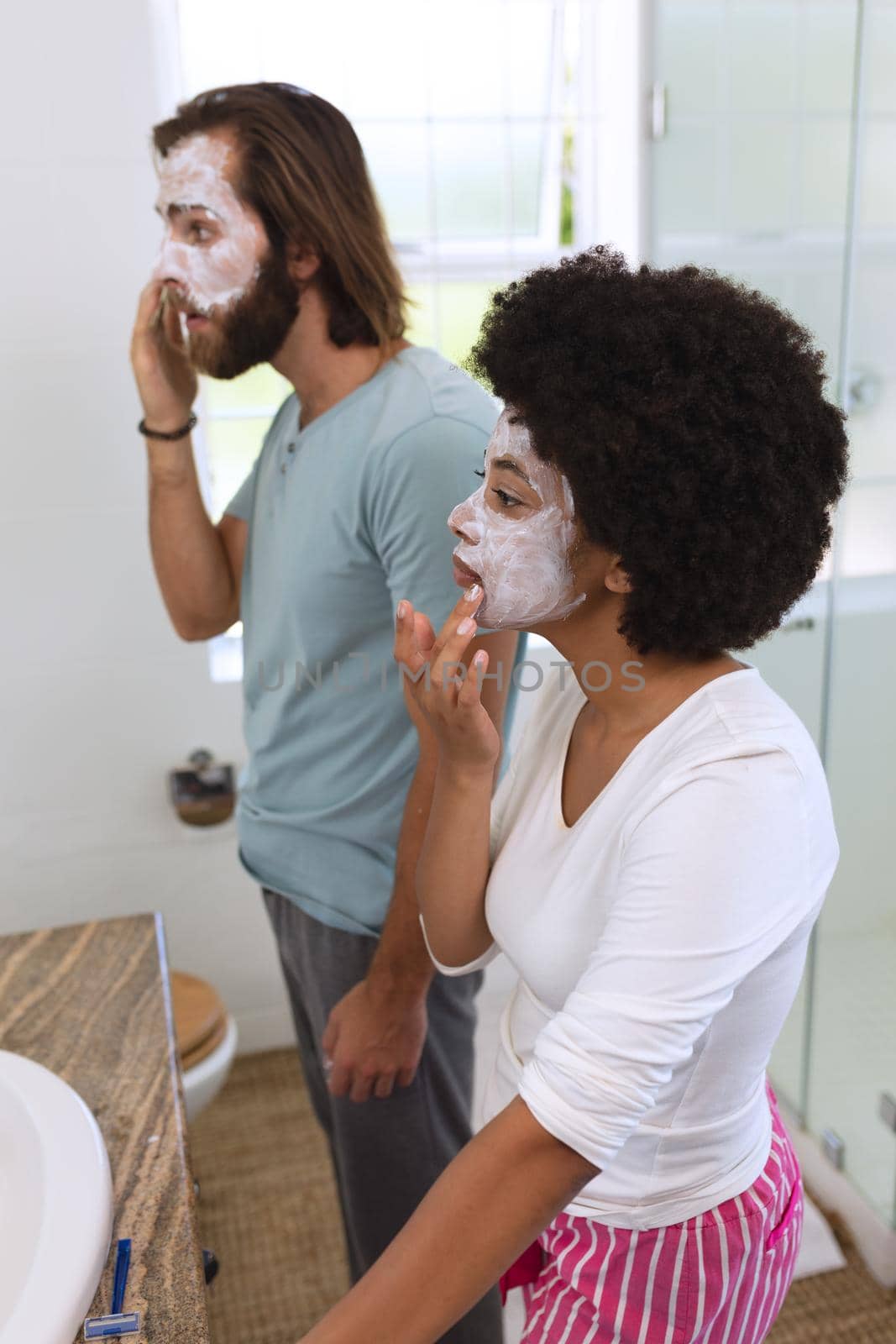 Diverse couple standing in bathroom wearing beauty masks. staying at home in isolation during quarantine lockdown.