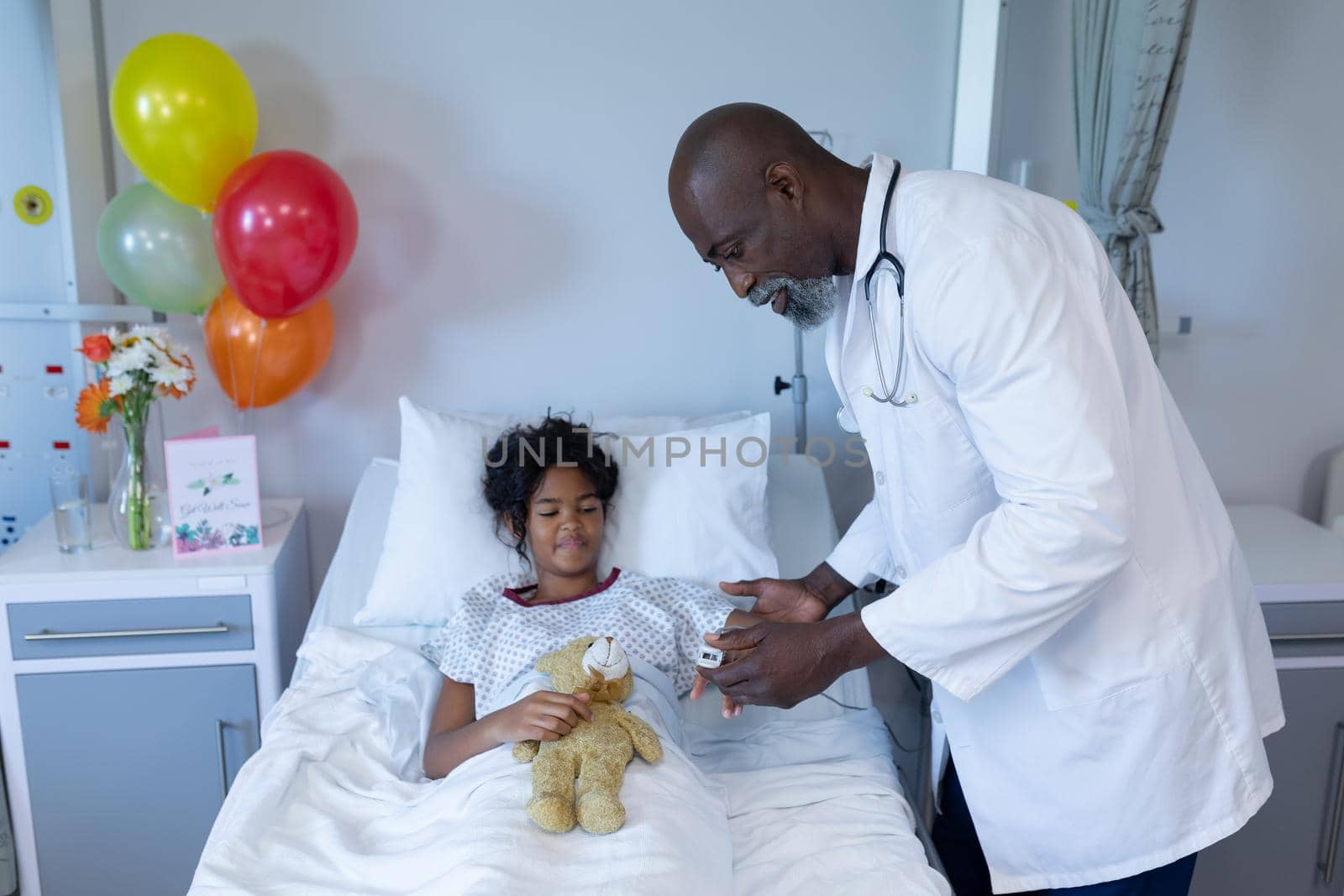 African american male doctor putting pulse oximeter on sick mixed race girl in hospital bed. medicine, health and healthcare services.