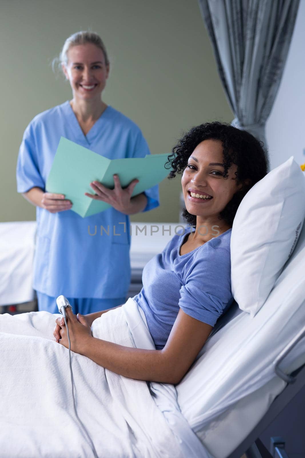 Portrait of smiling caucasian female doctor and mixed race patient sitting up in hospital bed. medicine, health and healthcare services.