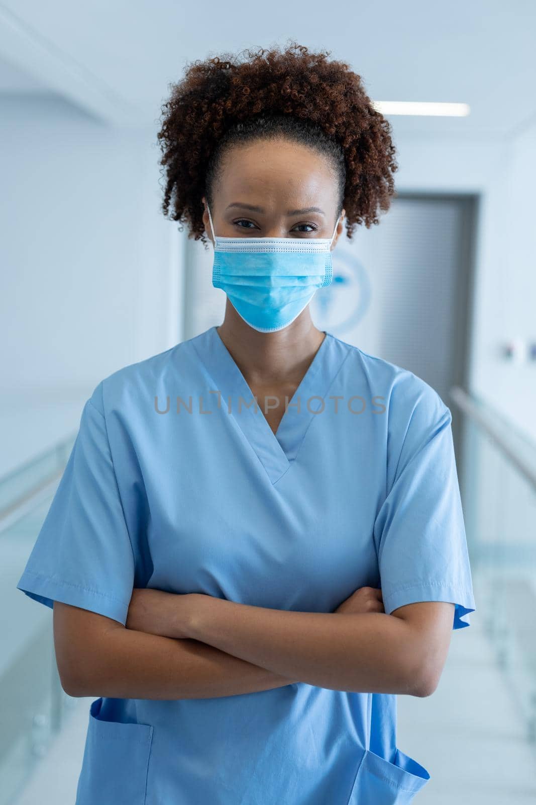 Portrait of african american female doctor wearing mask standing in hospital corridor. medicine, health and healthcare services during coronavirus covid 19 pandemic.