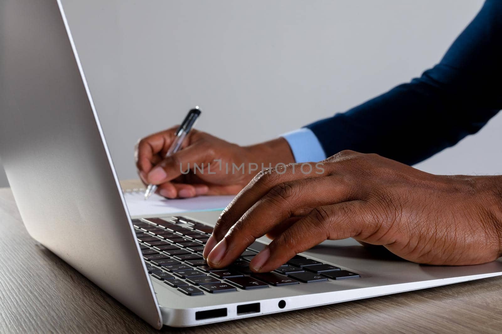 Close up of businessman using laptop and taking notes against grey background. business, professionalism and technology concept