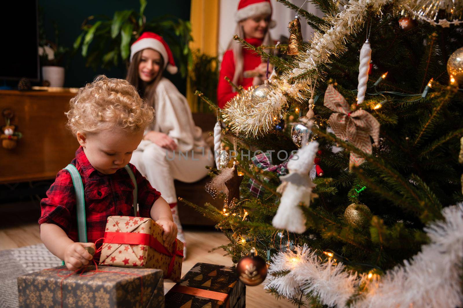 A two-year-old child looks at wrapped gift boxes standing next to a Christmas tree. Traditional Christmas in Poland.