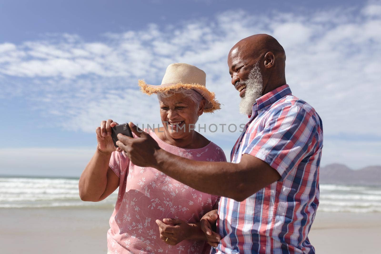 Happy senior african american couple using smartphone at the beach. travel vacation retirement lifestyle concept