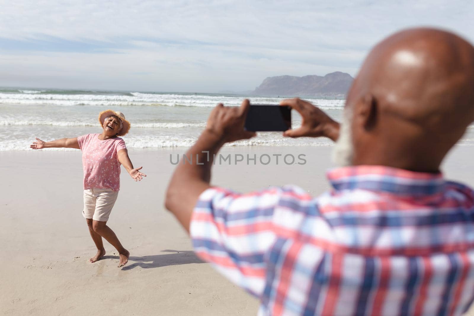 Senior african american man taking a picture of his wife on the beach by Wavebreakmedia