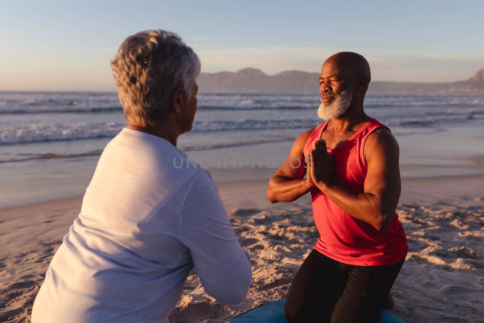 Senior african american couple with folded hands meditating and practicing yoga together at the beach. fitness yoga and healthy lifestyle concept