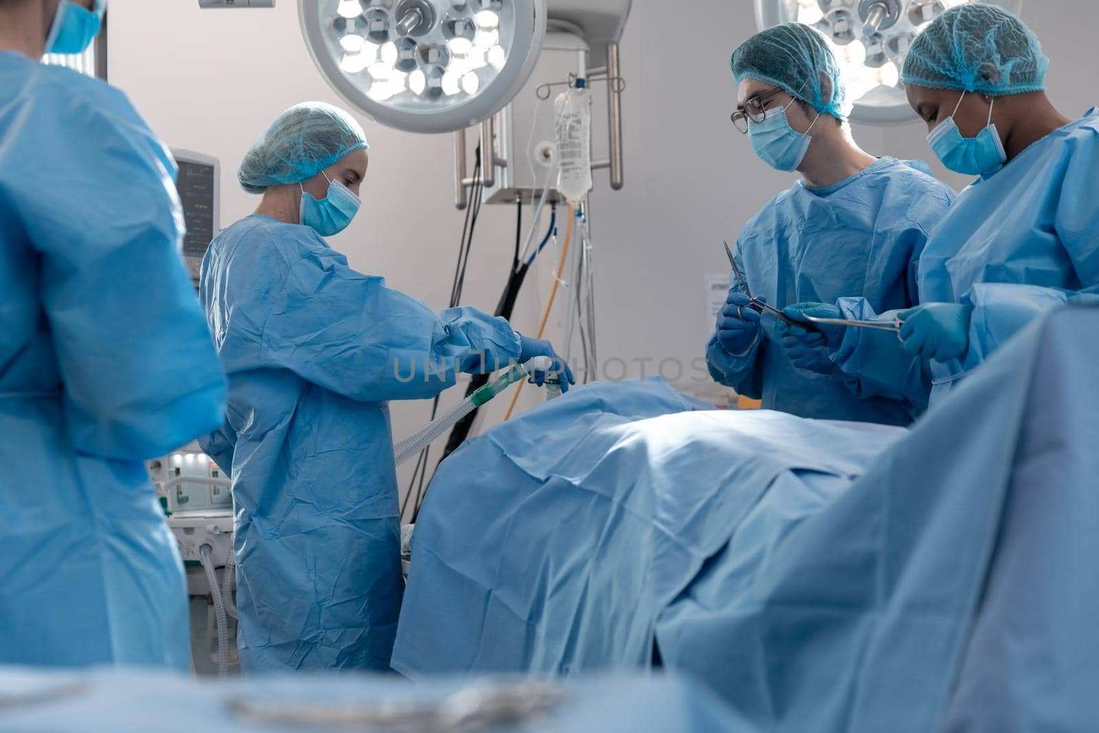 Diverse group of male and female surgeons in operating theatre wearing face masks performing surgery. medicine, health and healthcare services during coronavirus covid 19 pandemic.