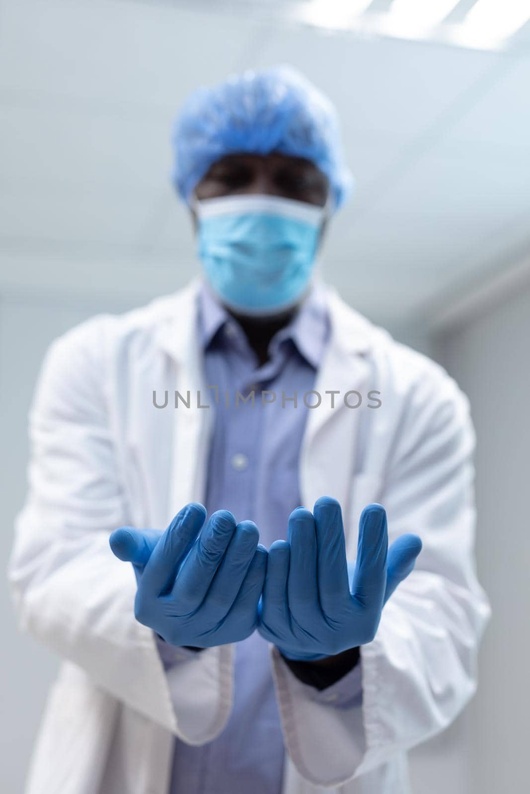 Portrait of african american male doctor wearing face mask surgical cap and latex gloves by Wavebreakmedia