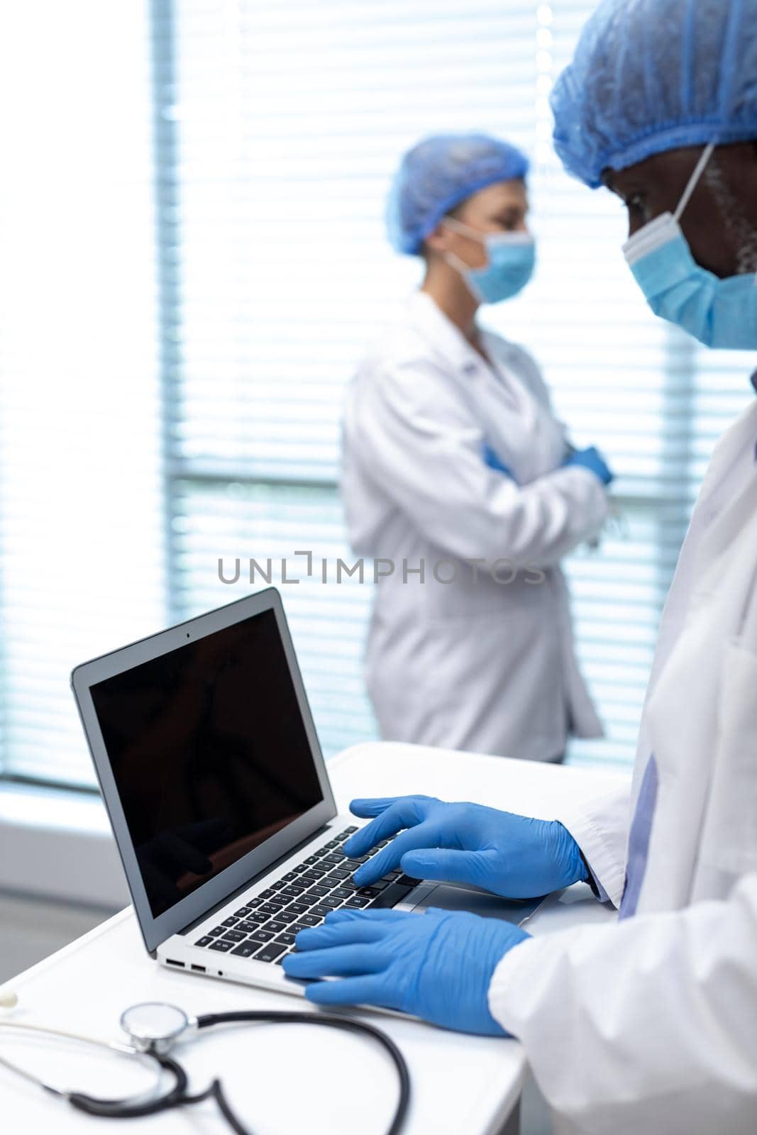 African american male doctor wearing mask and latex gloves using laptop with copy space on screen by Wavebreakmedia