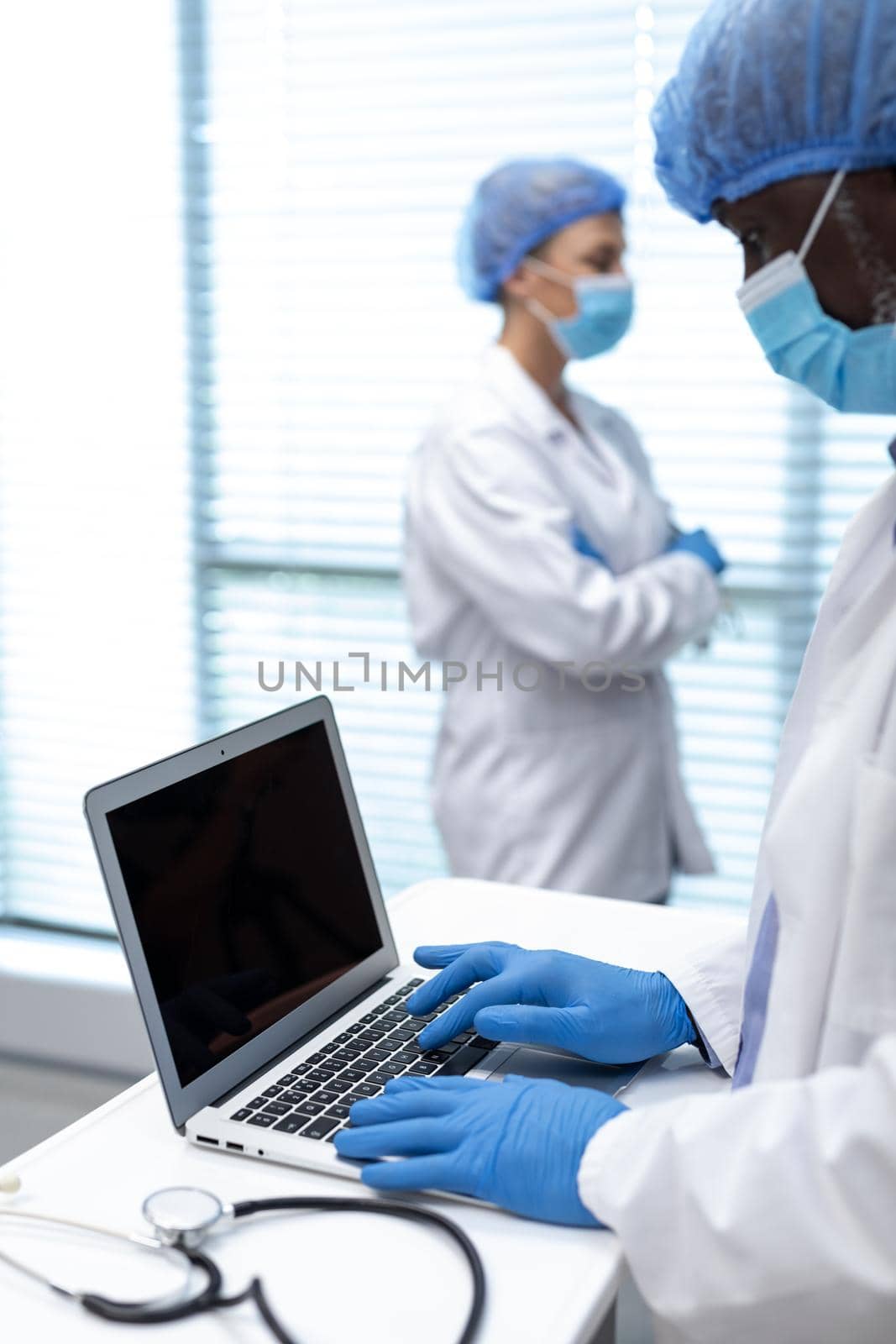 African american male doctor wearing mask and latex gloves using laptop with copy space on screen. medicine, health and healthcare services during coronavirus covid 19 pandemic. .