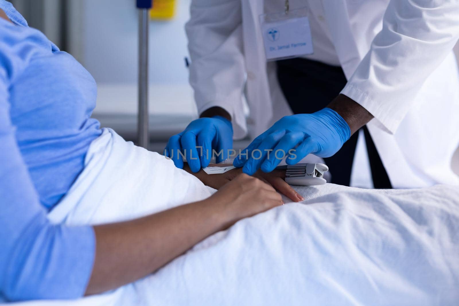 Midsection of african american male doctor preparing iv tube of female patient in hospital bed. medicine, health and healthcare services during coronavirus covid 19 pandemic.