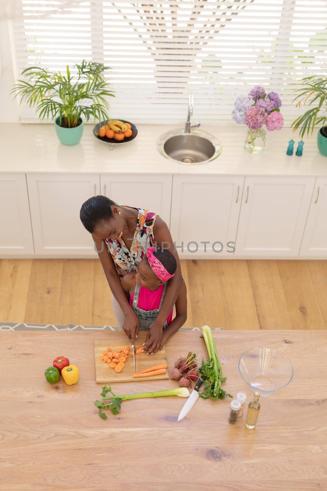 High angle view of african american mother teaching daughter cooking in the kitchen. staying at home in isolation during quarantine lockdown.