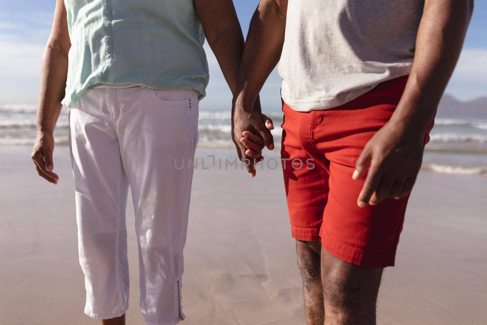 Mid section of african american couple holding hands standing on the beach by Wavebreakmedia