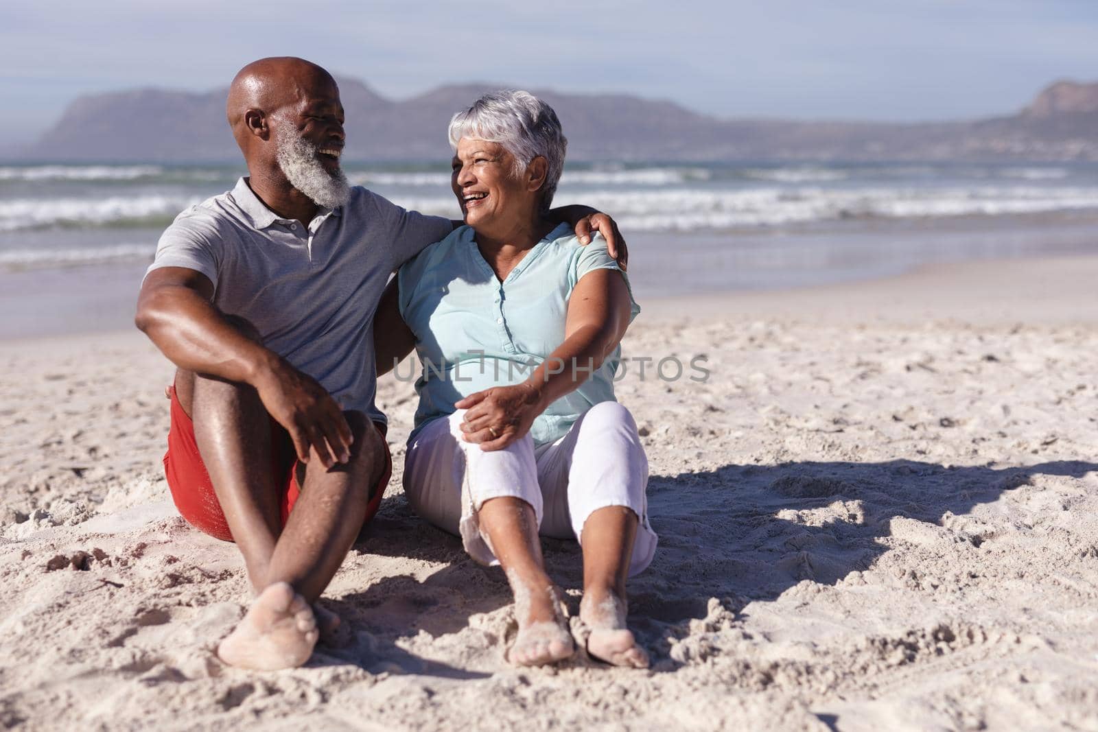 Senior african american couple smiling while looking at each other sitting on the beach by Wavebreakmedia