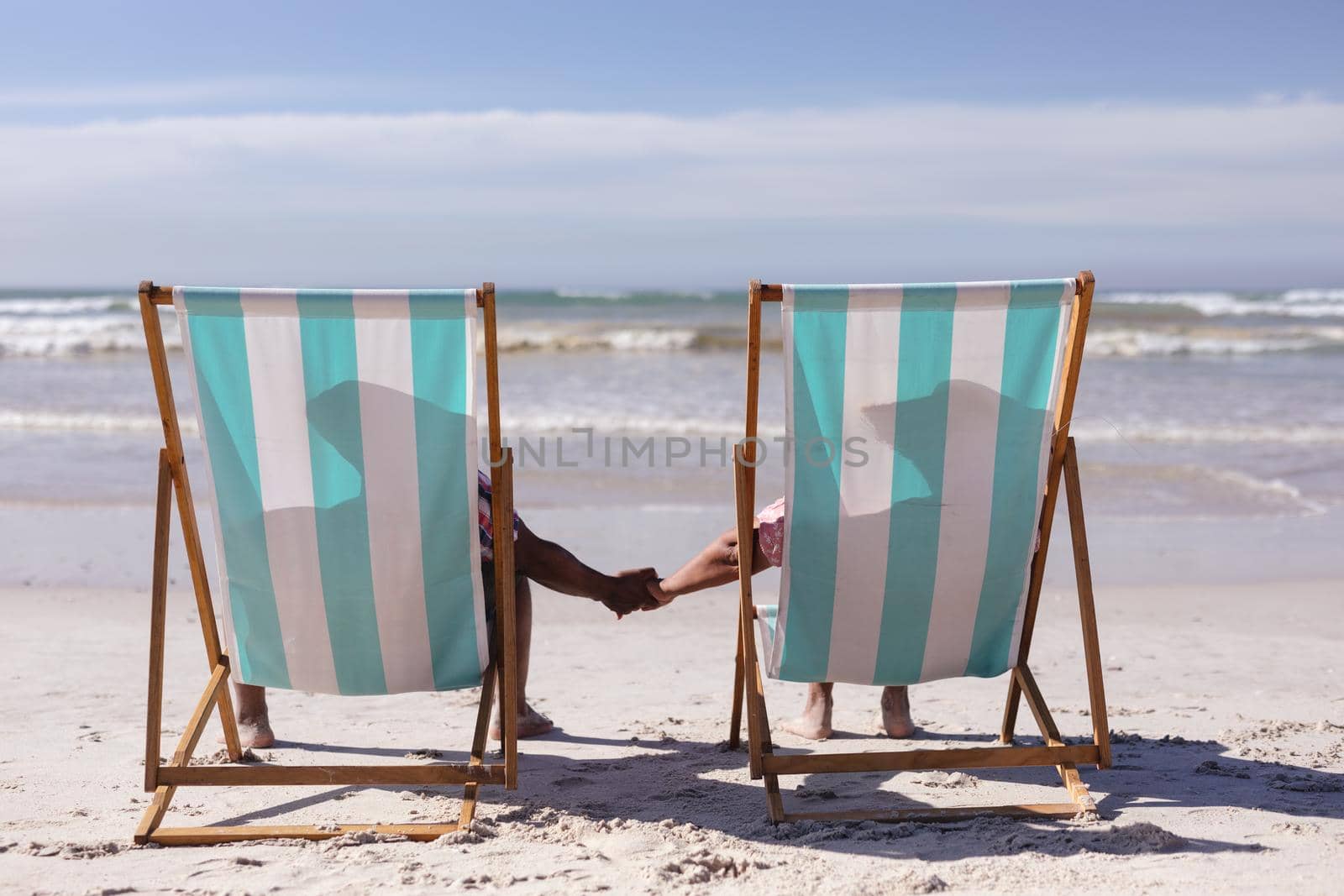 Rear view of senior african american couple holding hands while sitting on deck chairs at the beach by Wavebreakmedia