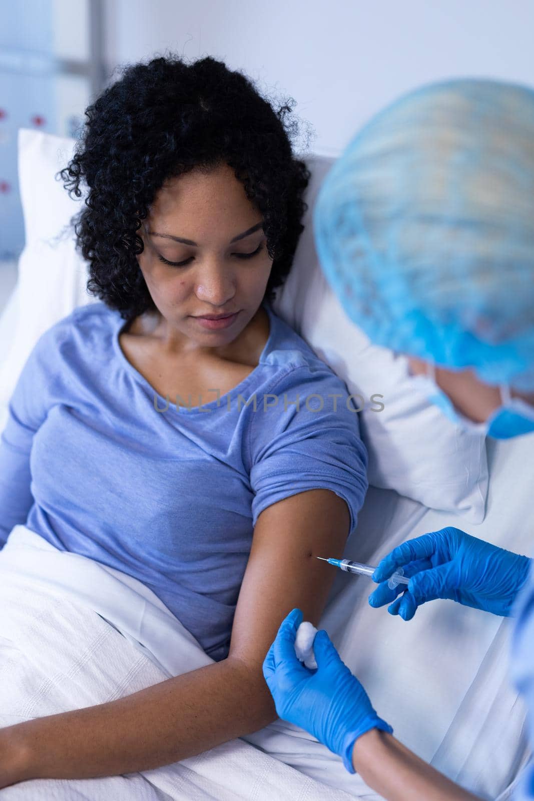 Caucasian female doctor in hospital wearing face mask vaccinating african american female patient. medical professional at work during coronavirus covid 19 pandemic.