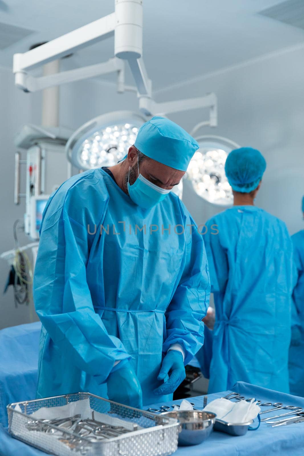 Caucasian male surgeon wearing face mask and protective clothing in operating theatre. medicine, health and healthcare services during covid 19 coronavirus pandemic.