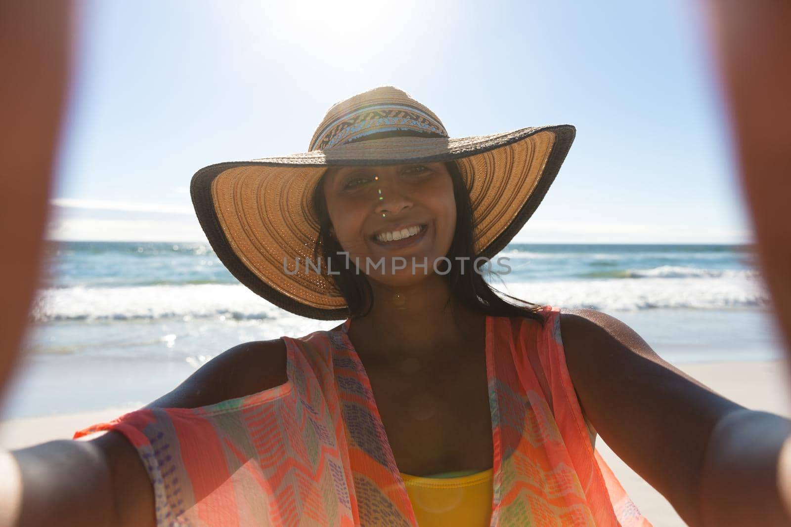 Smiling mixed race woman on beach holiday taking selfie. outdoor leisure vacation time by the sea.