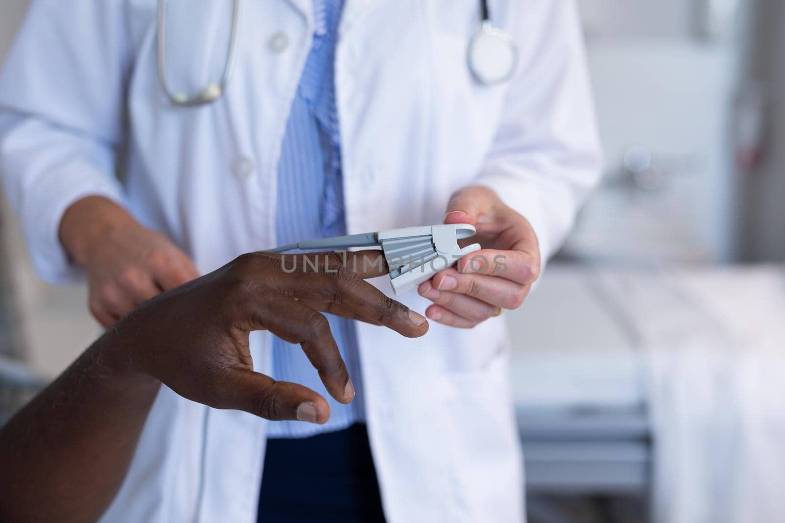 Midsection of diverse female doctor and male patient attaching pulse oximeter on finger. medicine, health and healthcare services.