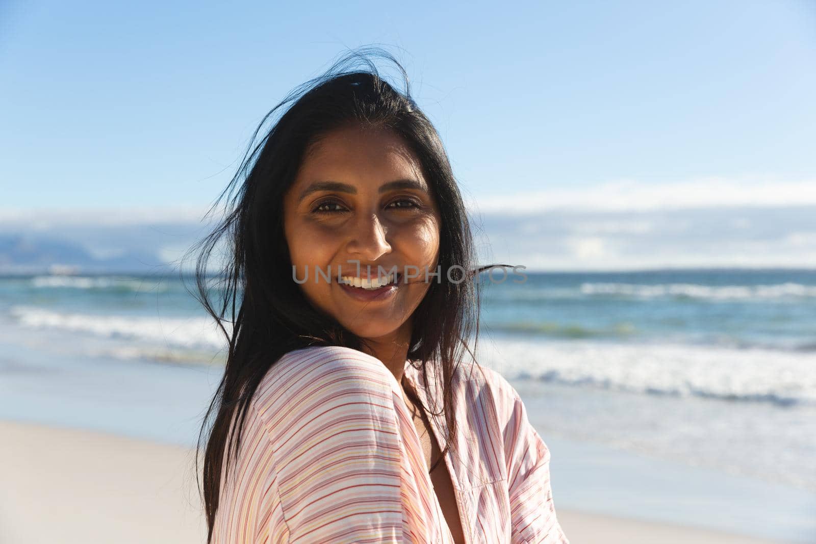 Portrait of smiling mixed race woman on beach holiday looking to camera. outdoor leisure vacation time by the sea.