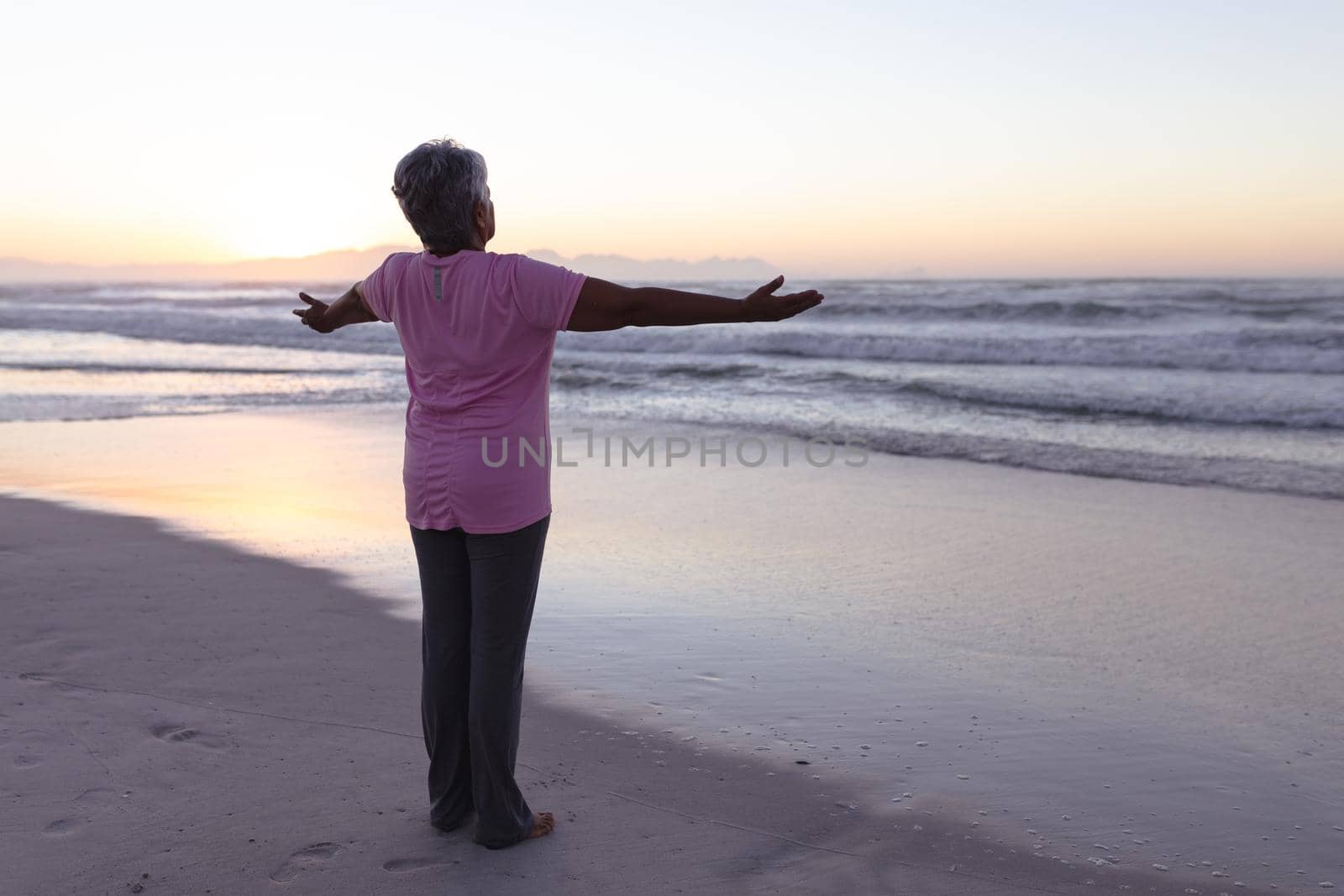 Rear view of senior african american woman standing with her arms wide open at the beach. travel vacation retirement lifestyle concept