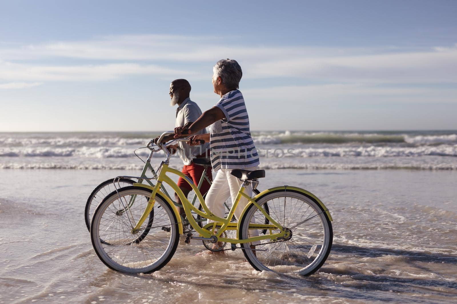 Happy senior african american couple with bicycles walking together on the beach. travel vacation retirement lifestyle concept