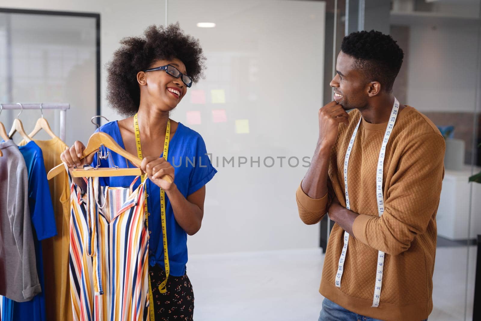 Diverse male and female fashion designers at work discussing and looking at clothes by Wavebreakmedia