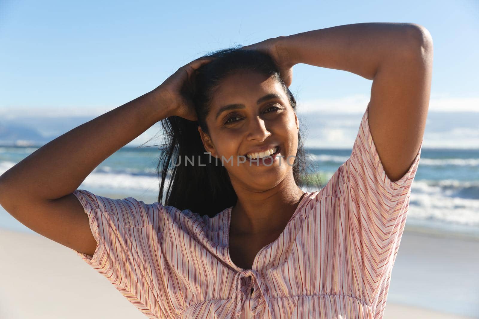 Portrait of smiling mixed race woman on beach holiday looking to camera. outdoor leisure vacation time by the sea.