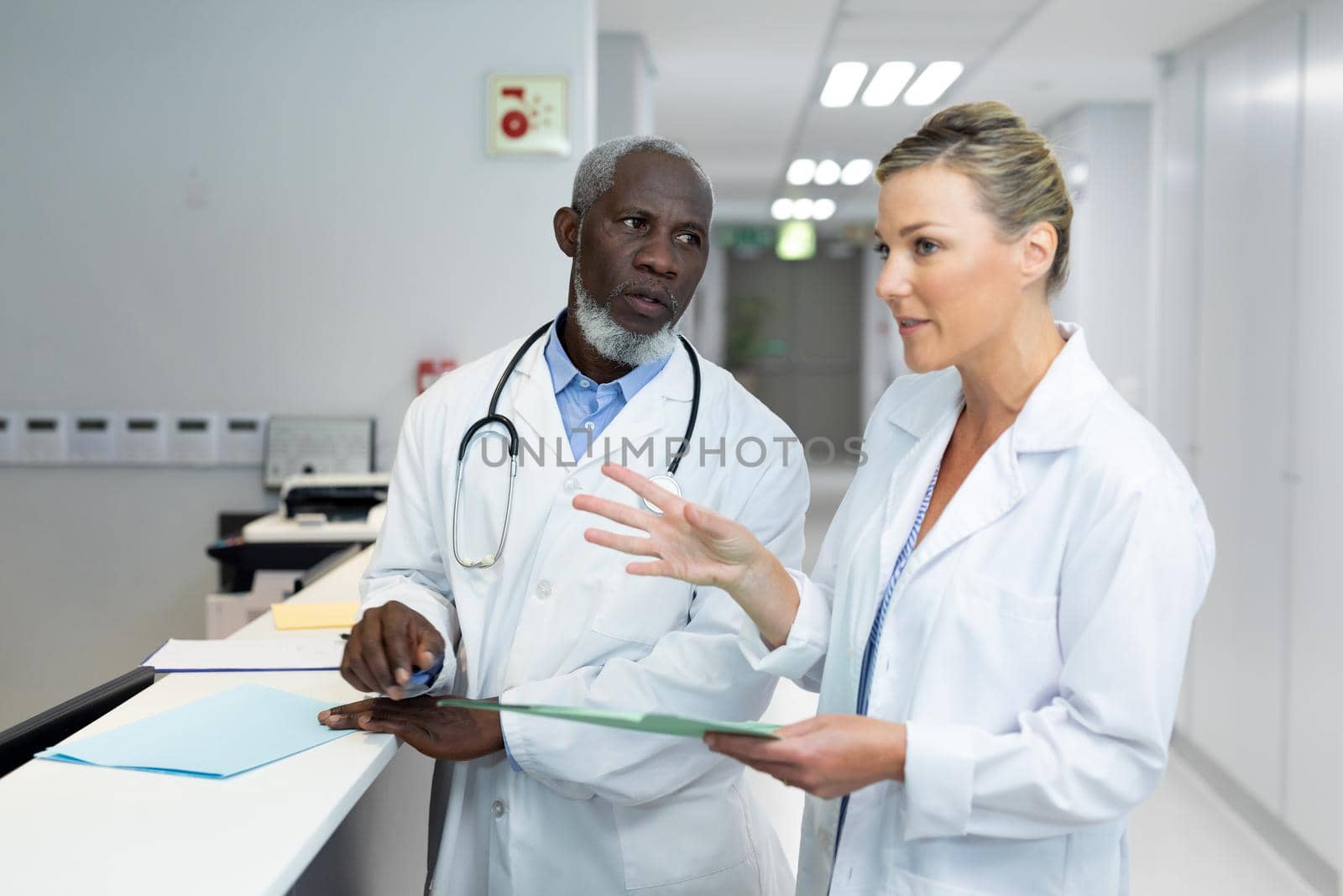 Diverse male and female doctors standing in hospital corridor talking by Wavebreakmedia