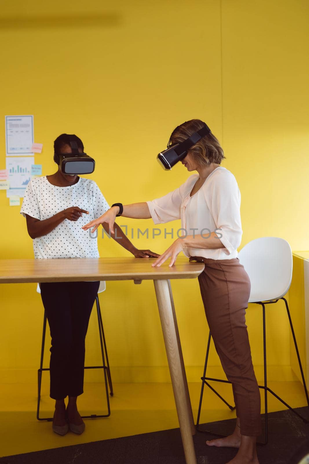 Diverse businesswomen standing at desk using vr headset at work by Wavebreakmedia