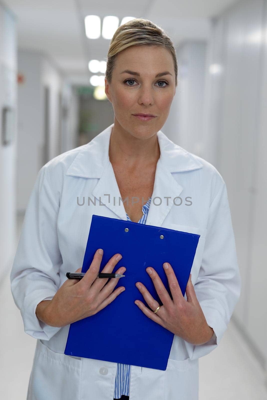 Portrait of caucasian female doctor standing in hospital corridor holding medical chart document by Wavebreakmedia