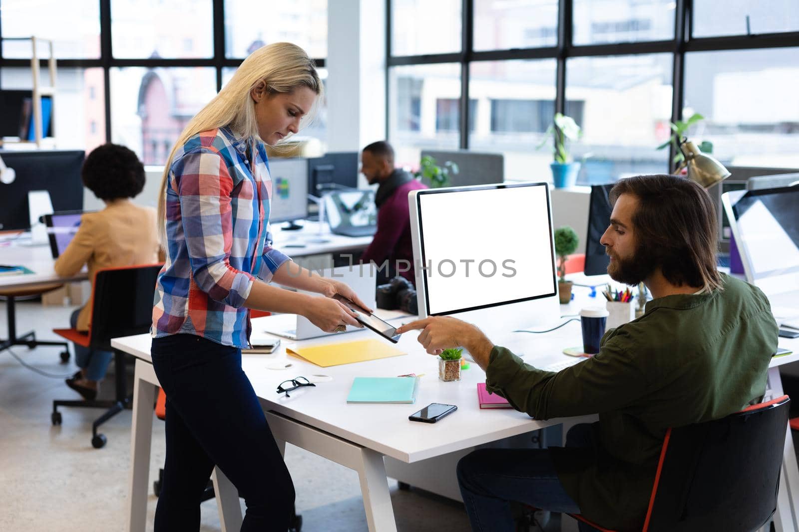 Caucasian business people working in creative office. man and woman using tablet computer, with colleagues in the background. business people and work colleagues at a busy creative office.