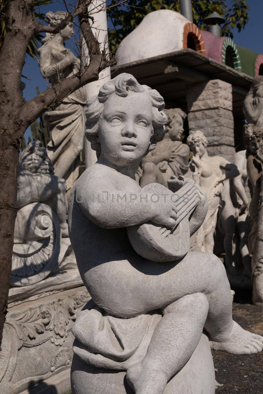 Ancient stone sculpture of naked cherub playing lute in reclamation yard. art and classical style romantic figurative stone sculpture.