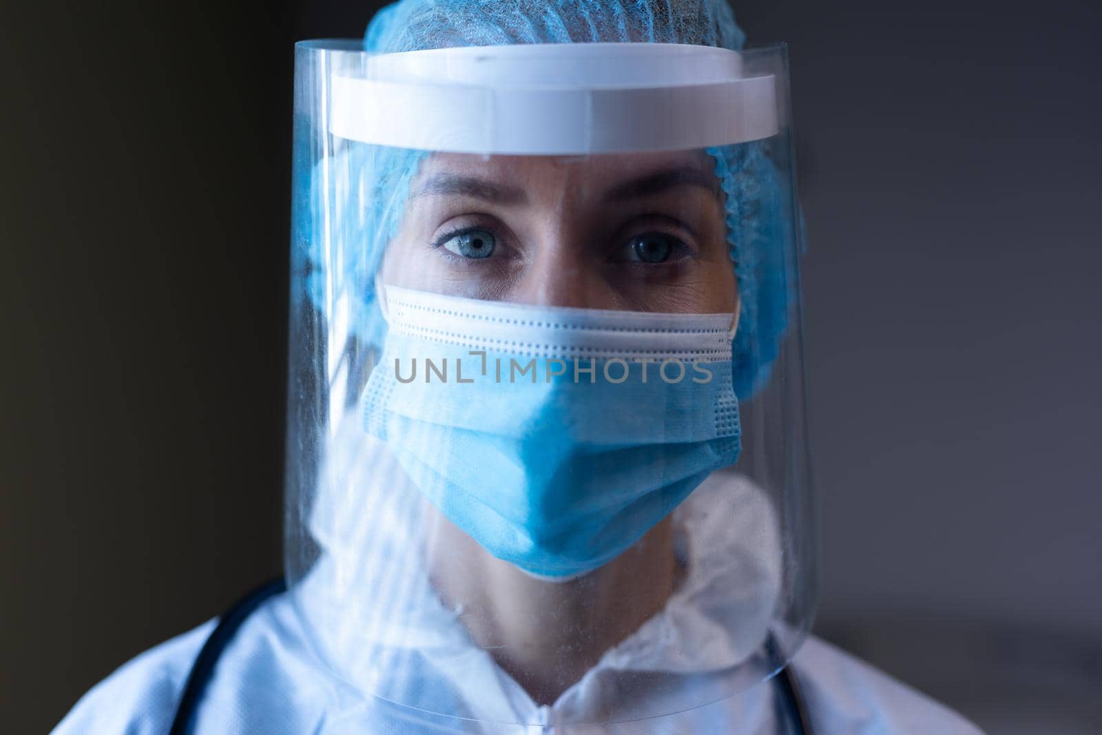 Caucasian female doctor in hospital wearing ppe suit, face mask, face shield and medical cap. medical professional at work and protective clothing during coronavirus covid 19 pandemic.
