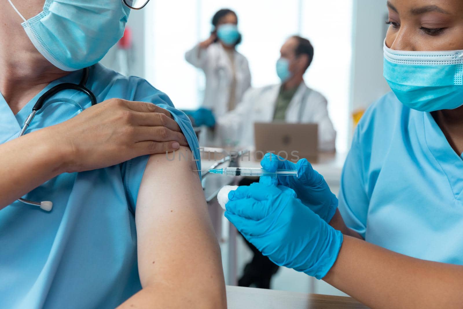 African american female doctor giving covid vaccination to male colleague, both in face masks by Wavebreakmedia