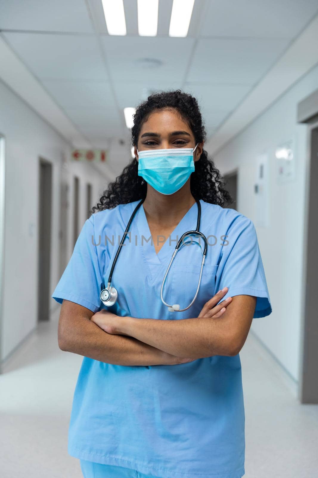 Portrait of mixed race female doctor wearing face mask standing in hospital corridor by Wavebreakmedia