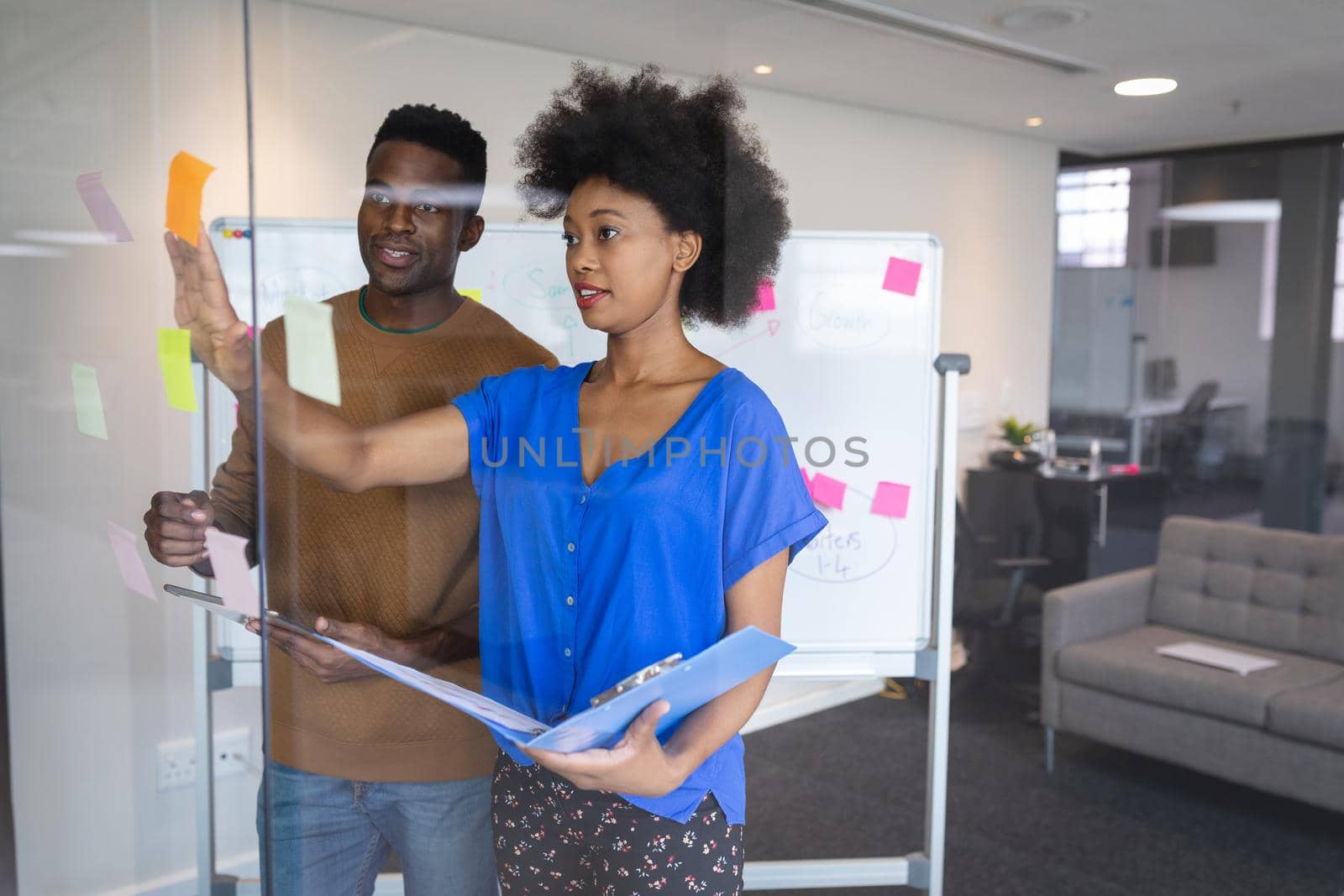 Diverse male and female colleagues standing having discussion with whiteboard in background. independent creative design business.