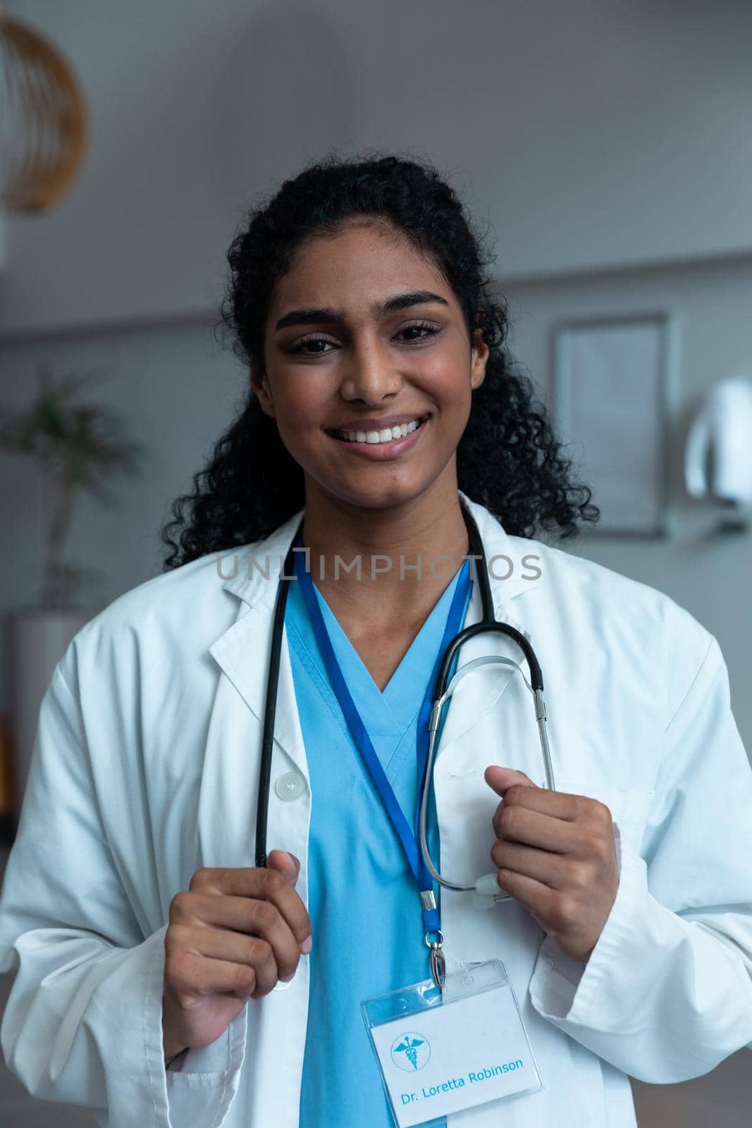Portrait of smiling mixed race female doctor with stethoscope wearing lab coat in hospital. medicine, health and healthcare services during covid 19 coronavirus pandemic.