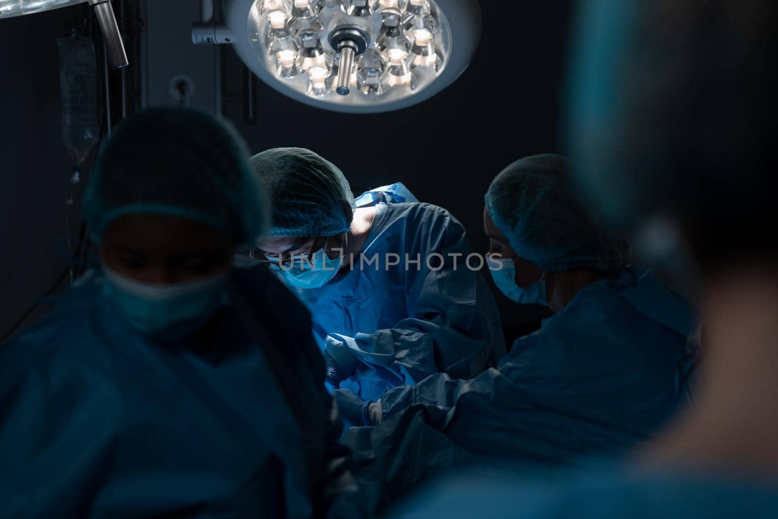 Diverse group of male and female surgeons in operating theatre wearing face masks performing surgery. medicine, health and healthcare services during coronavirus covid 19 pandemic.