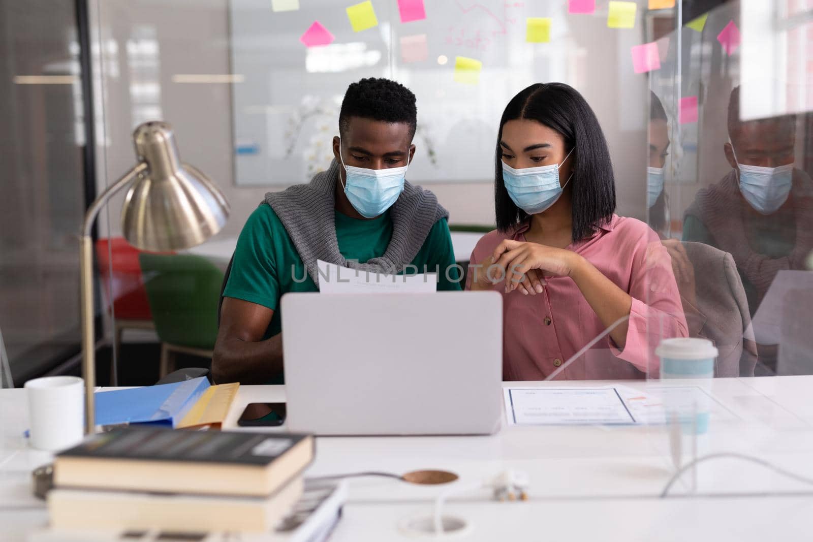 Diverse creative colleagues wearing face masks brainstorming in meeting room. independent creative design business during covid 19 coronavirus pandemic.