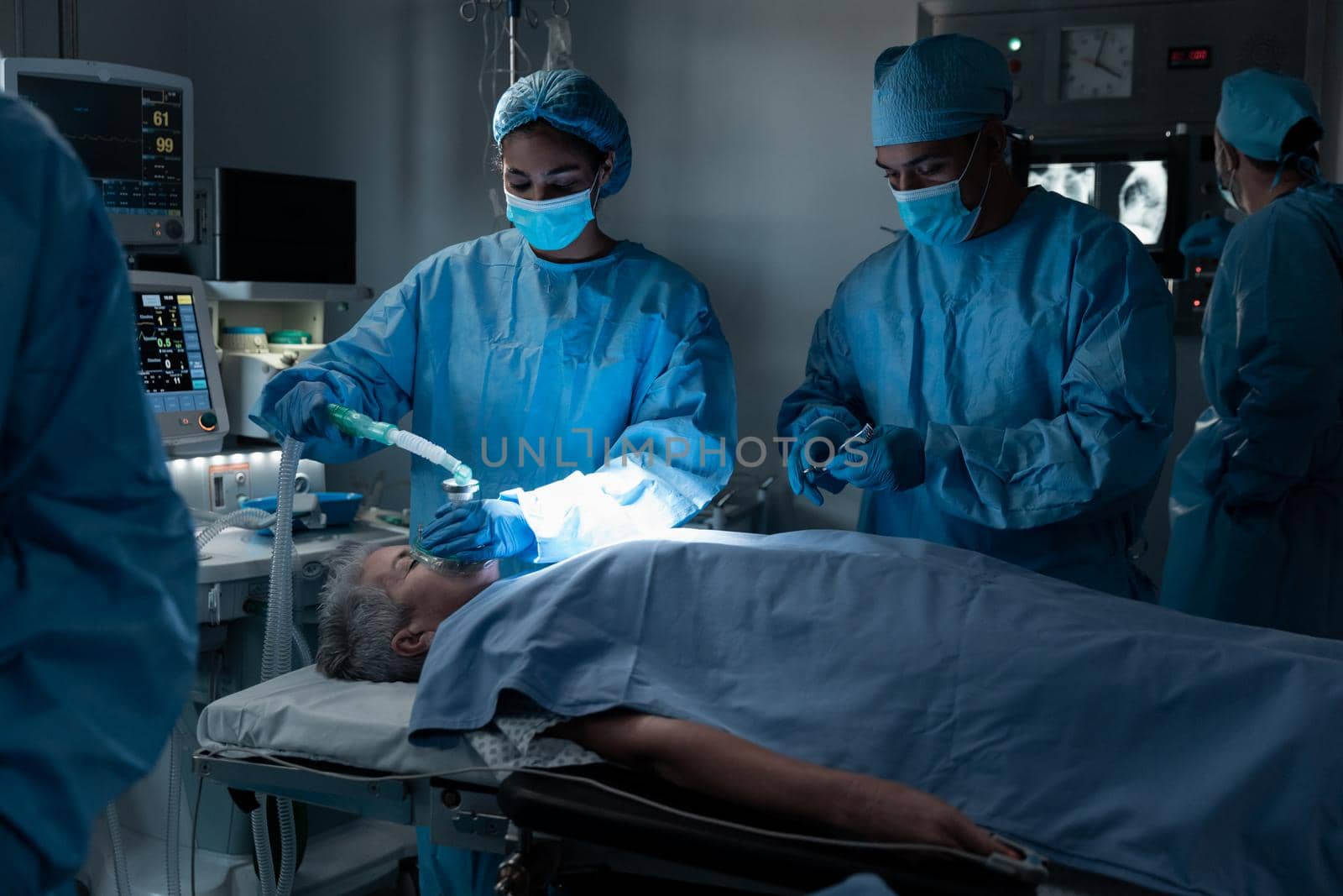 Diverse surgeons with face masks and protective clothing during operation, sedating patient by Wavebreakmedia