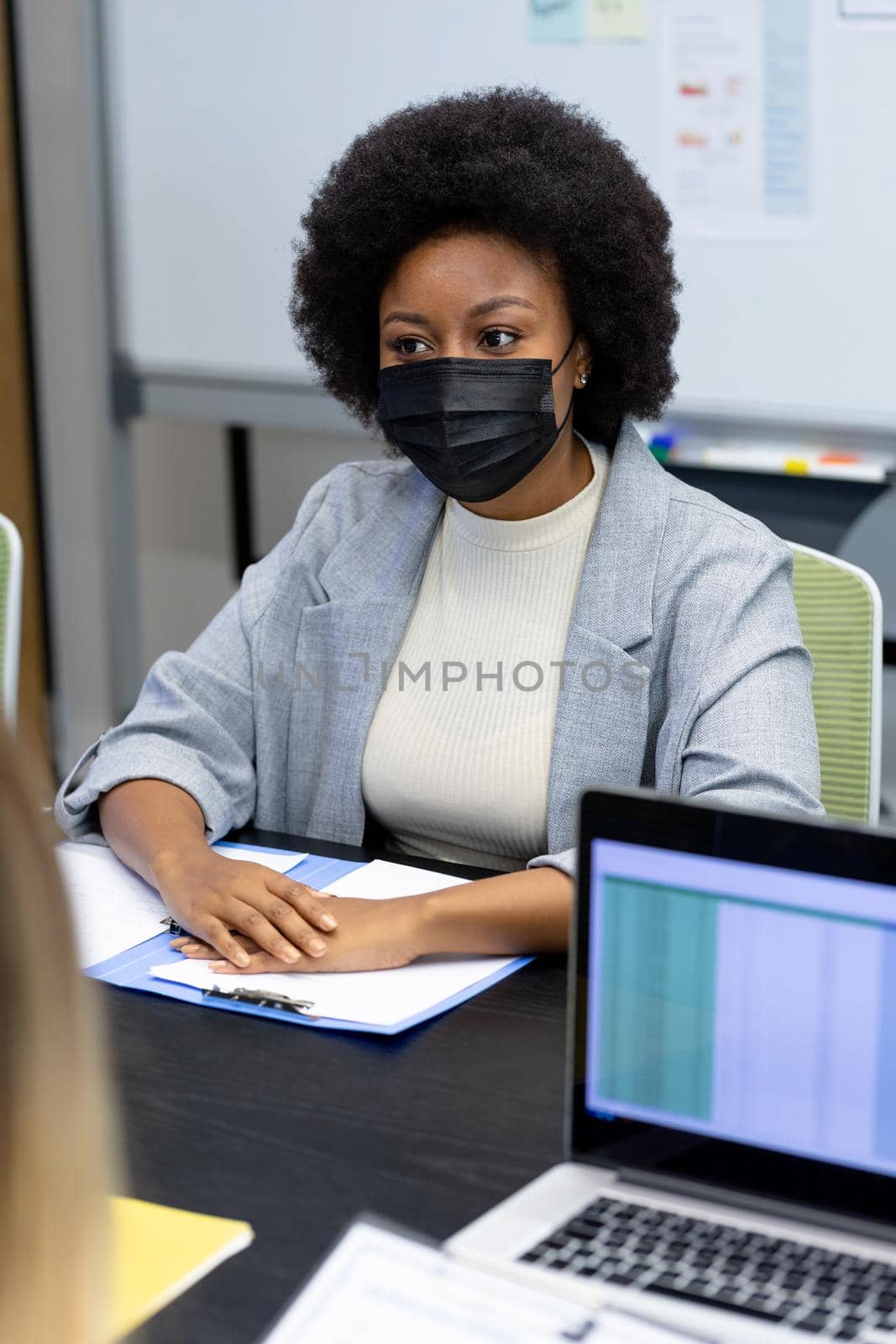 Portrait of african american businesswoman wearing face mask sitting at desk in meeting room by Wavebreakmedia