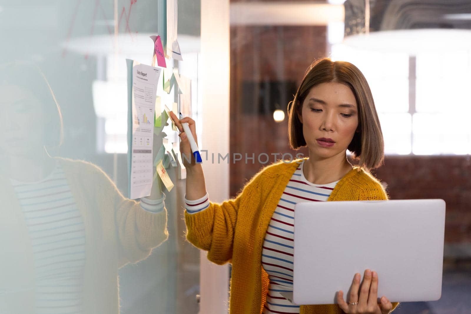 Asian businesswoman standing in front of whiteboard and writing holding laptop having video call. independent creative design business.