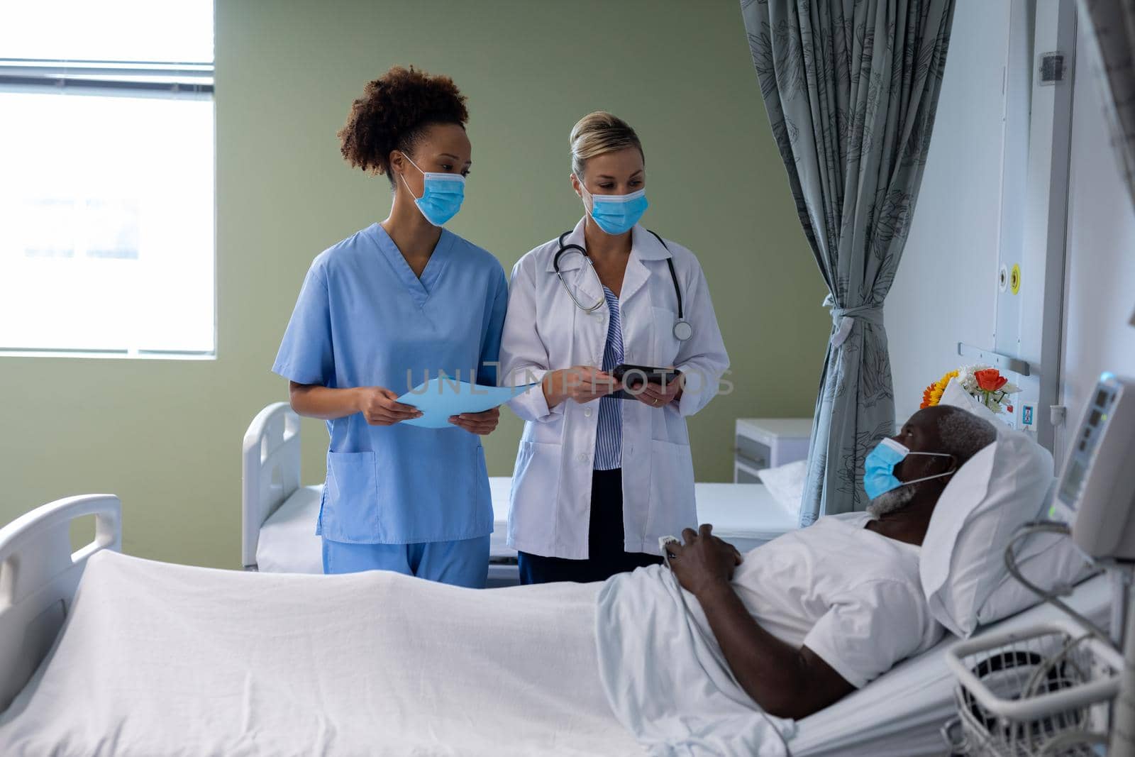 Two diverse female doctors wearing face masks talking with african american male patient by Wavebreakmedia