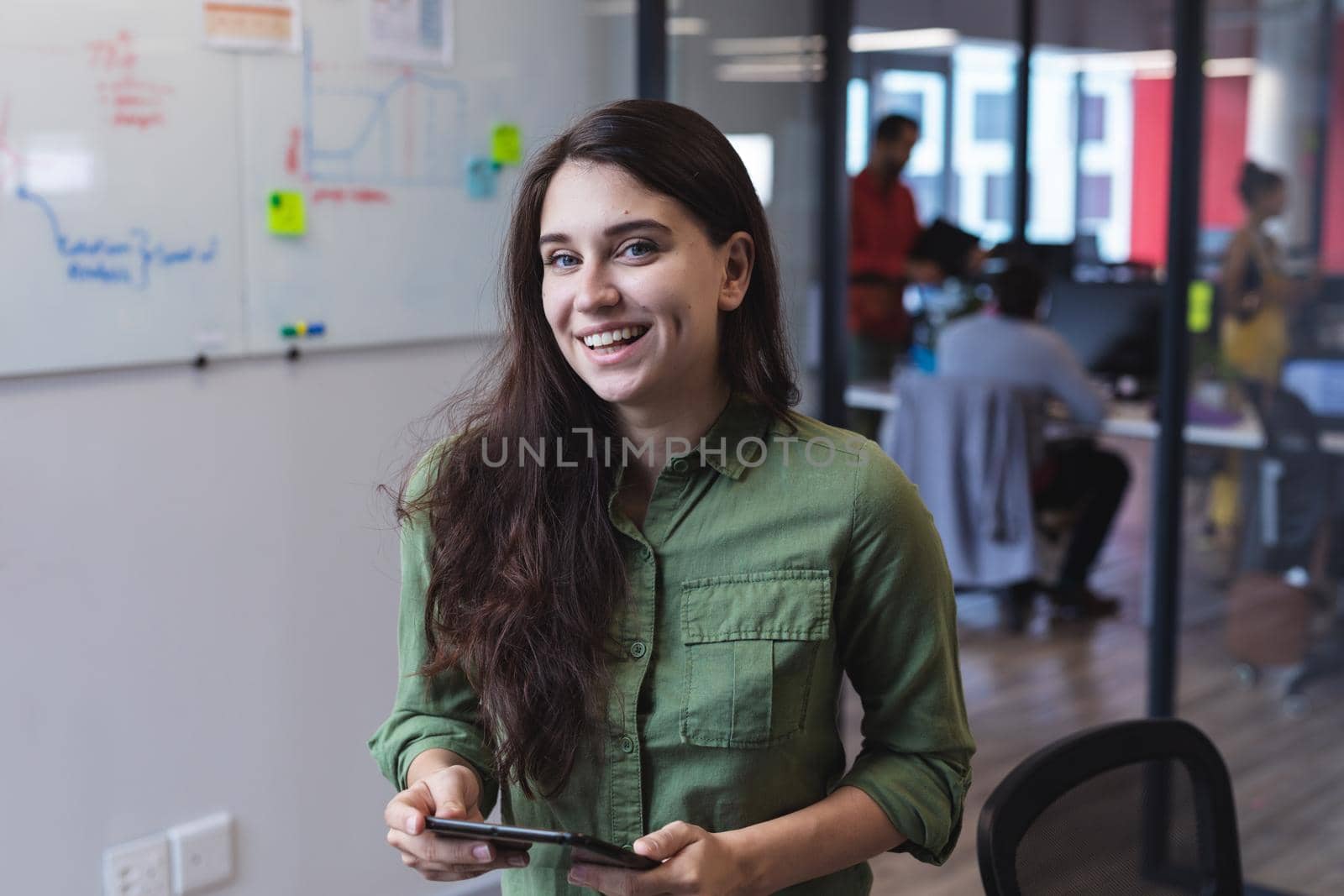 Portrait of caucasian female creative worker using tablet computer and looking at camera. modern office of a creative design business.